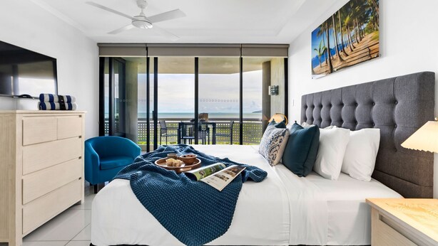 Ein Hotelzimmer mit Bett, blauem Sessel, Holzkommode und Balkon mit Meerblick.