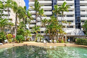 A hotel with a pool surrounded by palm trees and lounge chairs.