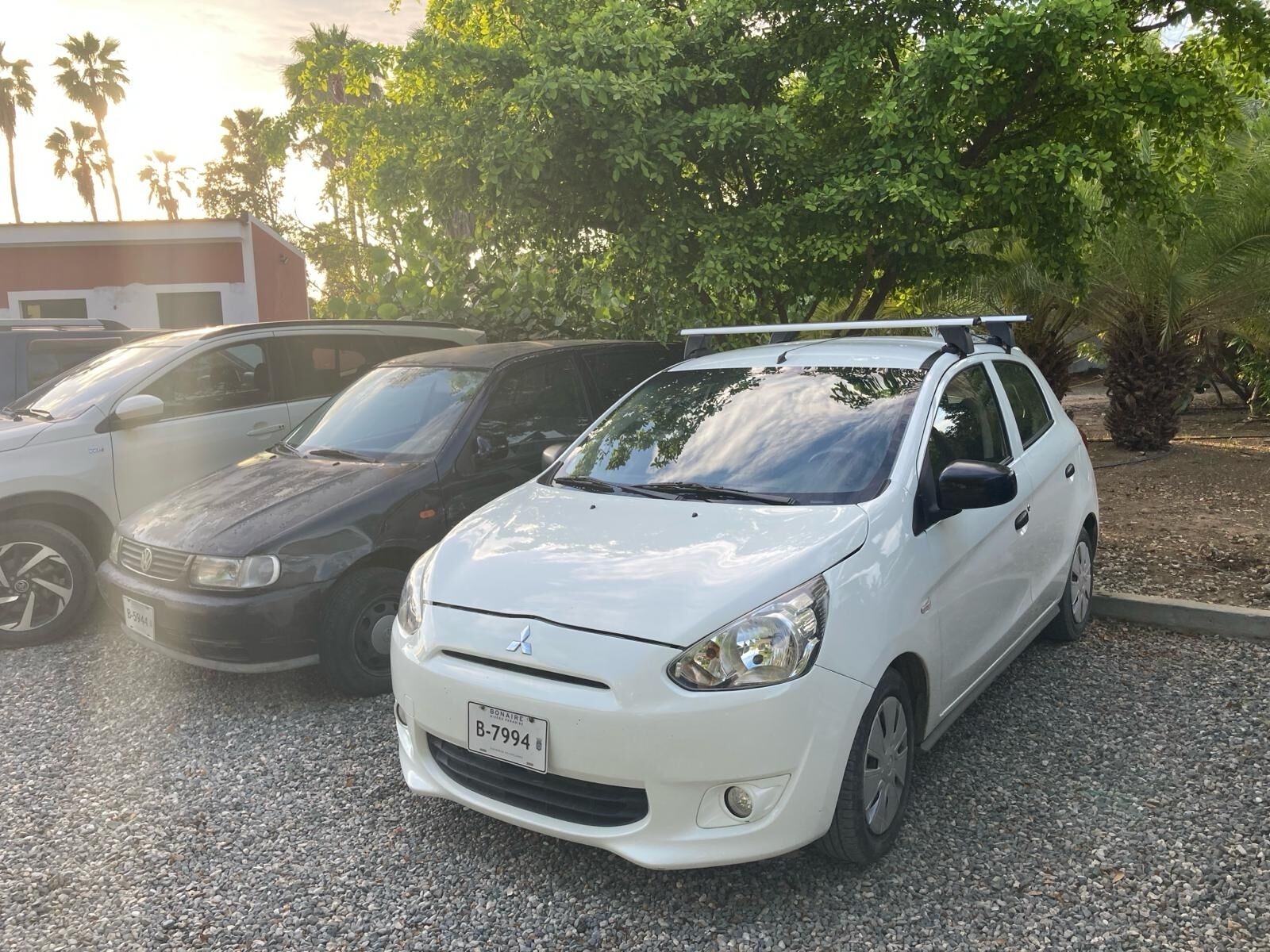 A white car with a roof rack parked on a gravel surface.