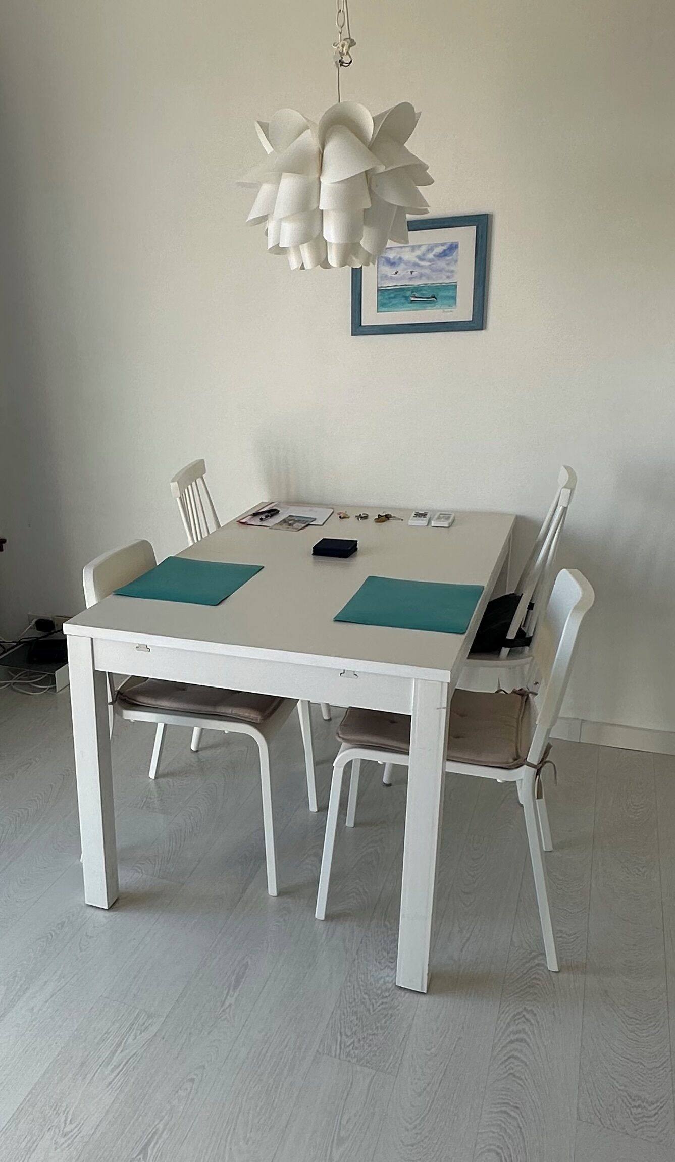 A dining table with four chairs, a hanging light fixture, and a framed picture on the wall.