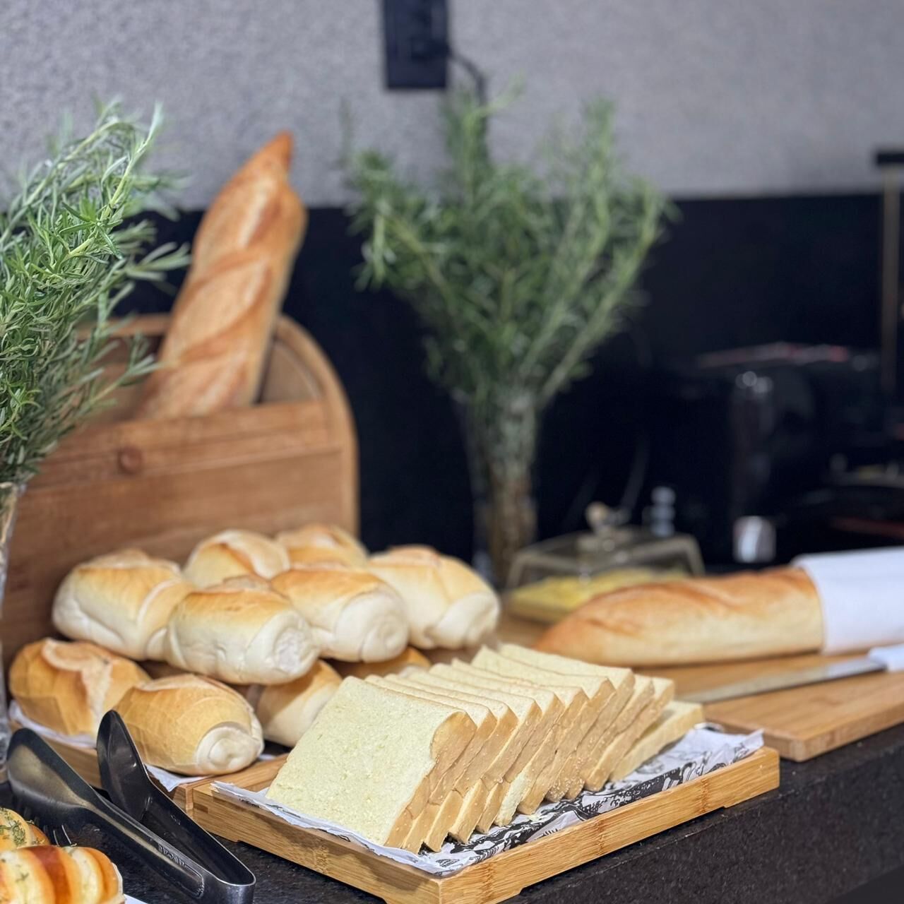 A variety of breads and pastries on a wooden board, with a knife and a cutting board nearby.