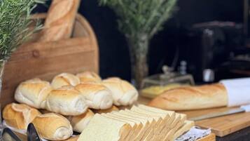 A variety of breads and pastries on a wooden board, with a knife and a cutting board nearby.
