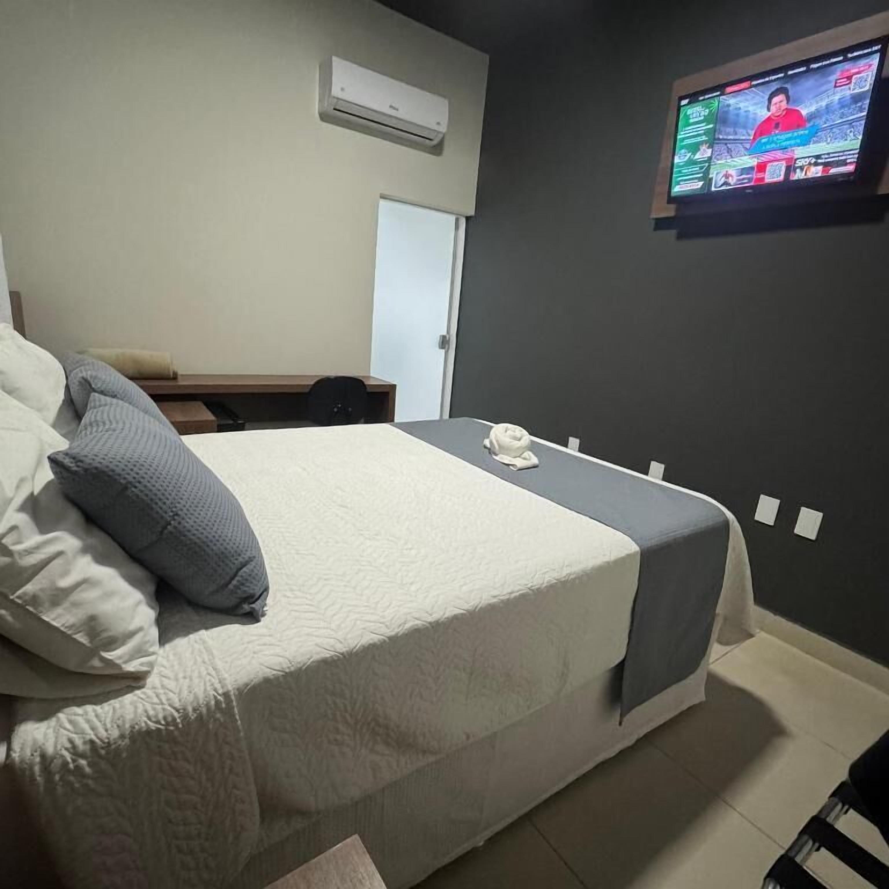 Een hotelkamer met een bed, een bureau, een stoel, een aan de muur bevestigde televisie en een deur.