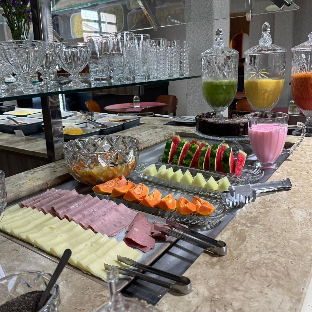 Un bufé con diversos alimentos y bebidas, como carnes frías, quesos, frutas y una variedad de jugos.