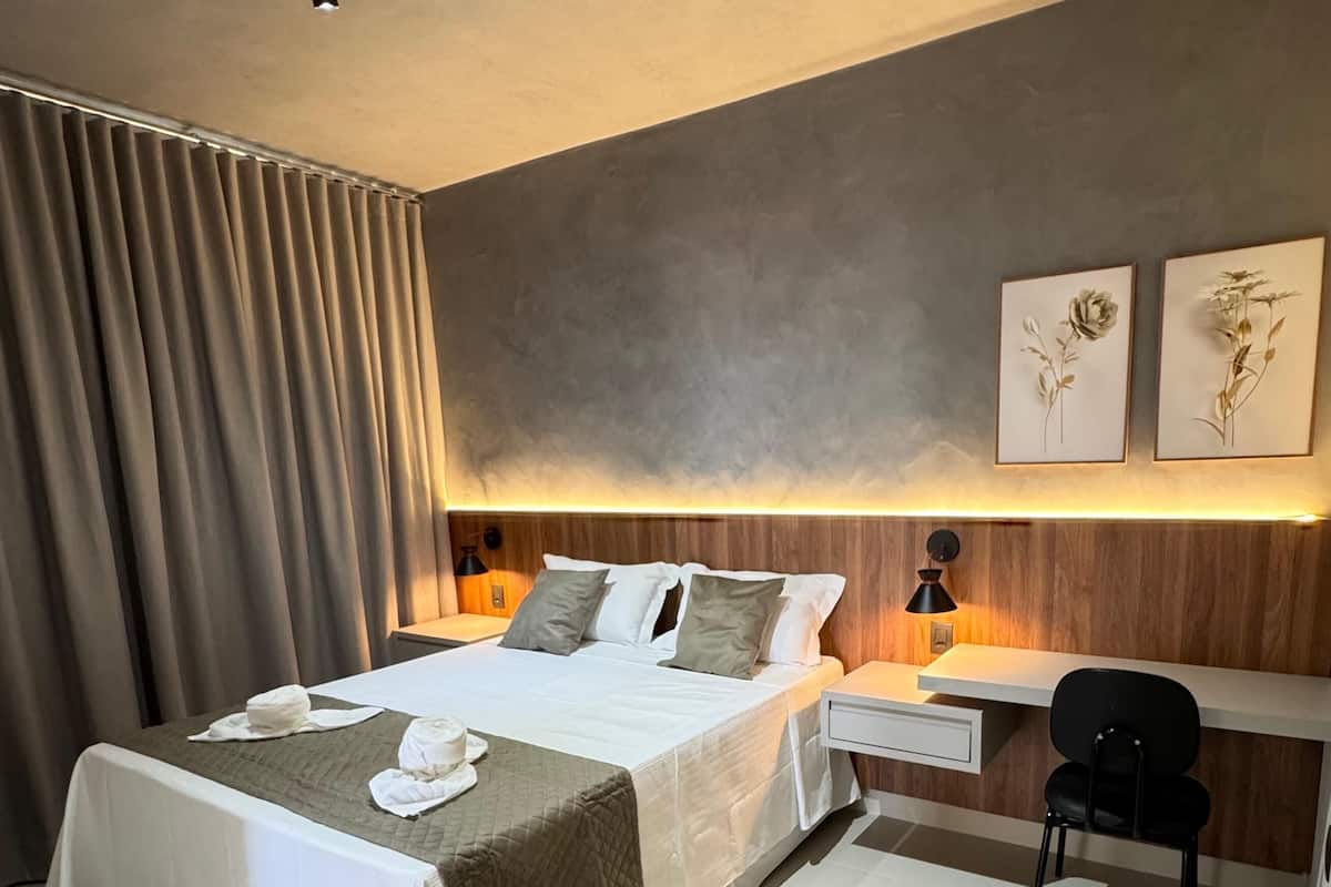A modern hotel room with a large bed, a desk, and two wall-mounted lamps.