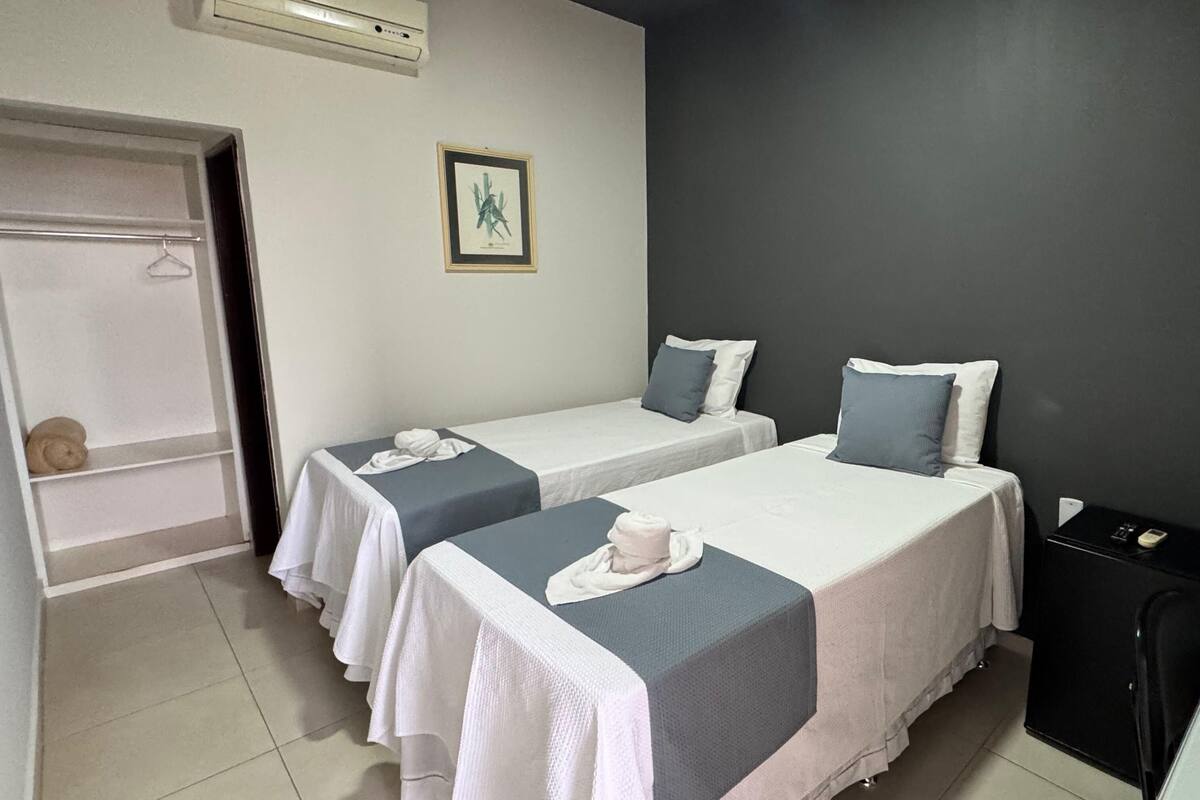 A hotel room with two single beds, a small desk, a wardrobe, and an air conditioning unit.
