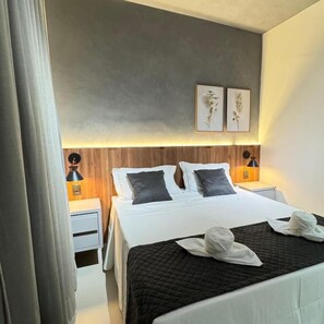 A hotel room with a large bed, two bedside tables with lamps, a wooden headboard, and two wall-mounted artworks. - POUSADA BRUMADO (Brumado)