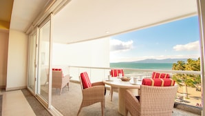 Un balcone con mobili in vimini, un tavolo e vista sull'oceano e sulle montagne.