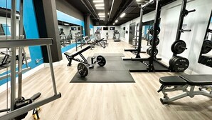 Een moderne sportschool met diverse fitnessapparaten, waaronder krachttrainingsmachines en losse gewichten, uitgestald op matten.