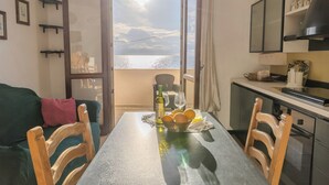 A dining area with a table set for two, a view of the sea through an open door, and a kitchen area with cabinets and a stove. - Casa Mare Torre San Carlo (Palma di Montechiaro)