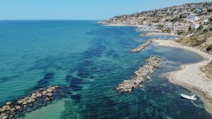 A coastal view with clear blue waters, a rocky breakwater, and a hillside settlement. - Casa Mare Torre San Carlo (Palma di Montechiaro)