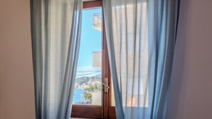 A window with sheer curtains, a view of a balcony with a railing, and a clear blue sky. - Casa Mare Torre San Carlo (Palma di Montechiaro)