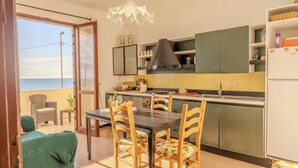 A kitchen with a view of the sea, a dining table with chairs, and a balcony with a chair and a sofa. - Casa Mare Torre San Carlo (Palma di Montechiaro)
