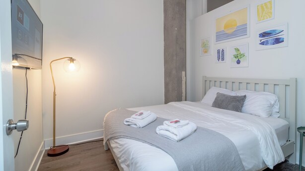 Une chambre d’hôtel avec un lit, une table de chevet, une lampe sur pied et des œuvres d’art accrochées au mur.