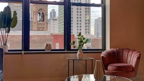 Une pièce avec une grande fenêtre, un fauteuil rouge, une petite table avec un vase et une plante en pot.