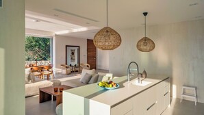 Een moderne keuken met een centraal eiland, hanglampen en een zithoek met een bank en stoelen.