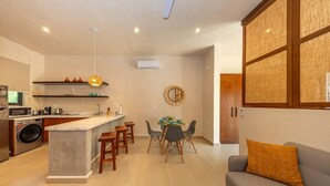 A modern kitchen with a central island, bar stools, and a dining area with a round table and chairs. - Lux 1 BR w/ Pool in Tulum Jungle @ Paraiso (Tulum)