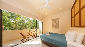 A bedroom with a bed, a ceiling fan, a window with a view of trees, and a small table with chairs. - Lux 1 BR w/ Pool in Tulum Jungle @ Paraiso (Tulum)