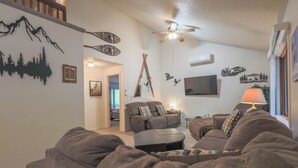 Ein Wohnzimmer mit einer Couch, einem Relaxsessel, einem Couchtisch, einem Deckenventilator und Wanddekorationen.