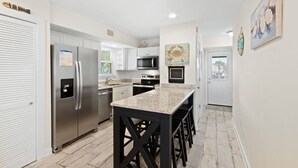 A modern kitchen with stainless steel appliances, a granite countertop, and a black bar stool seating area. - Laguna Bella B5 | Pool View (Gulf Shores)