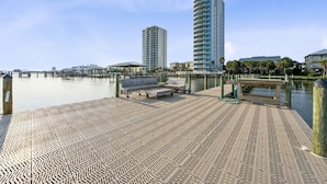 A waterfront promenade with a patterned walkway, benches, and a tall building in the background. - Laguna Bella B5 | Pool View (Gulf Shores)