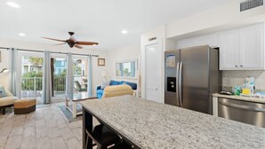 A modern kitchen with a granite countertop, stainless steel appliances, and a ceiling fan. - Laguna Bella B5 | Pool View (Gulf Shores)