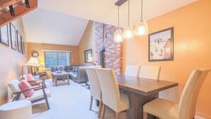 A dining area with a wooden table and chairs, a lamp, and a framed picture on the wall. - Official Seasons RMC Condo 09G - 2 bedrooms + loft - sleeps 10 - No Fees (Bartlett)