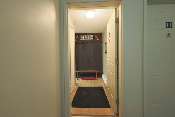 A hallway with a wooden bench, a black mat at the entrance, and a sign indicating 'Ski Slopes' direction. - Official Seasons RMC Condo 11G - 2 bedrooms + loft - sleeps 10 - No Fees (Bartlett)