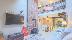 A living room with a fireplace, a TV mounted on the wall, a sofa, and a staircase leading to an upper level. - Official Seasons RMC Condo 11G - 2 bedrooms + loft - sleeps 10 - No Fees (Bartlett)
