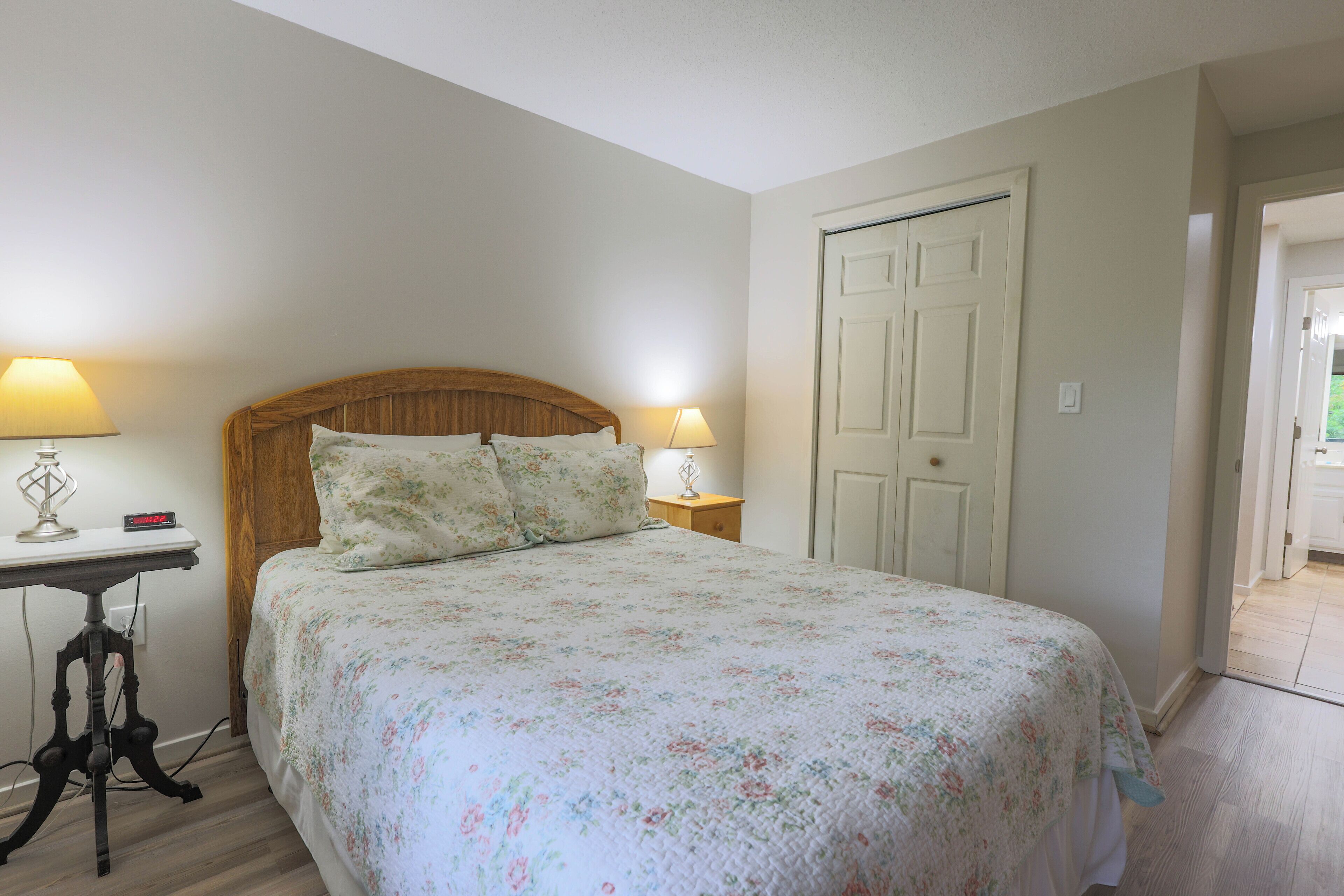 Un dormitorio con cama, dos mesitas de noche con lámparas, cabecera de madera y una puerta blanca.