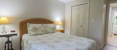 Un dormitorio con cama, dos mesitas de noche con lámparas, cabecera de madera y una puerta blanca.