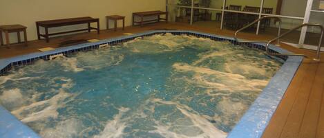 A hot tub with a wooden deck and a glass wall in the background.