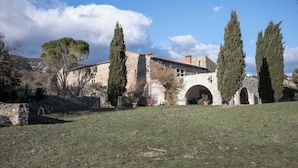 A stone building with a courtyard, featuring an arched entrance and tall cypress trees. - 3-star gîte rental at the foot of the Cévennes in a beautiful old farmhouse, sleeps 12. (Saint-André-de-Buèges)