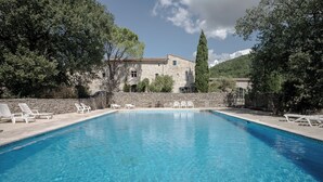 A swimming pool with lounge chairs, a stone building, and trees in the background. - 3-star gîte rental at the foot of the Cévennes in a beautiful old farmhouse, sleeps 12. (Saint-André-de-Buèges)