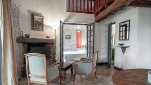 A room with a fireplace, two wooden chairs, a round table, and a view of a bedroom through an open door. - 3-star gîte rental at the foot of the Cévennes in a beautiful old farmhouse, sleeps 12. (Saint-André-de-Buèges)