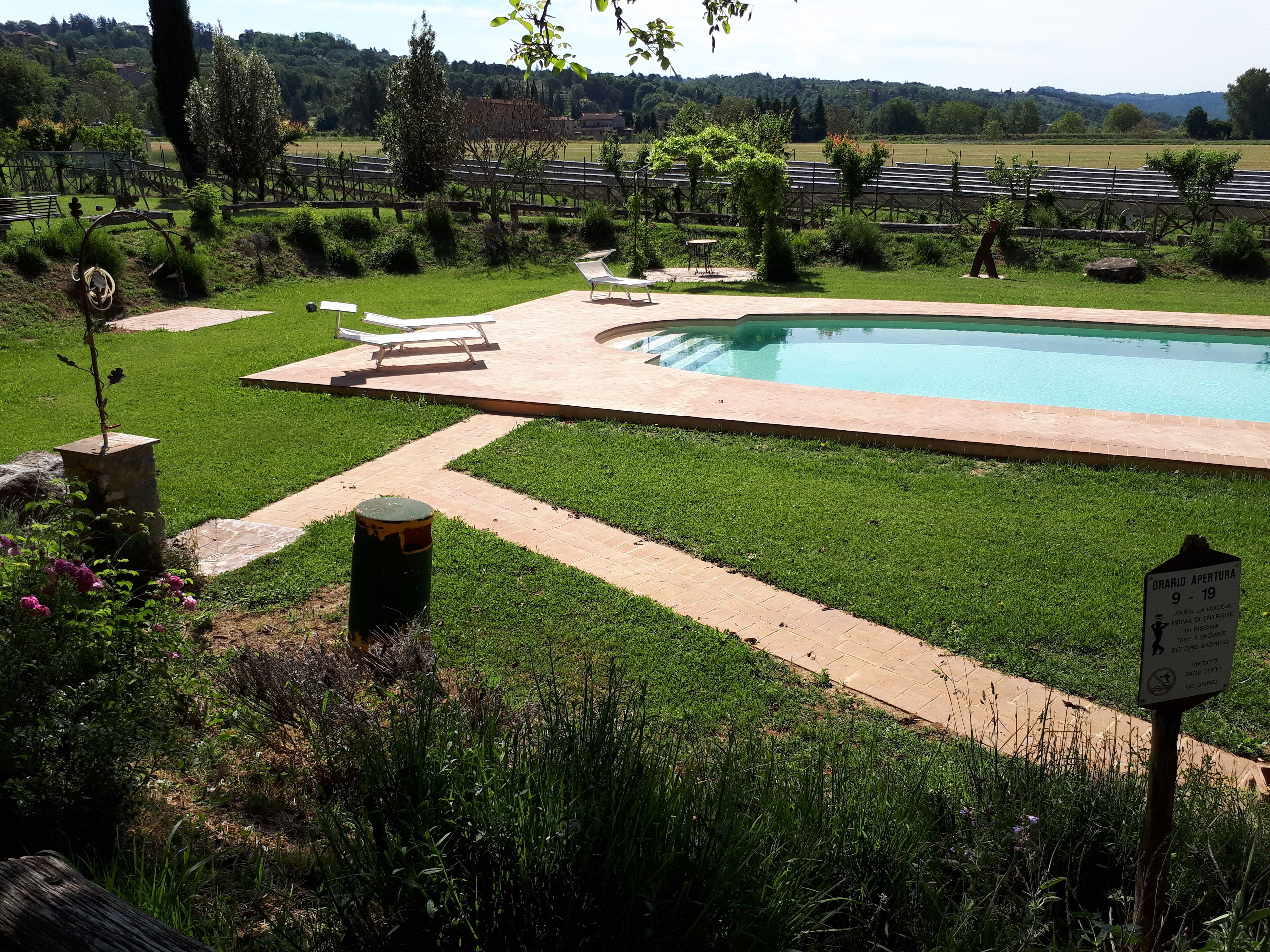 A pool area with a sign indicating the pool's opening hours and a warning against diving.