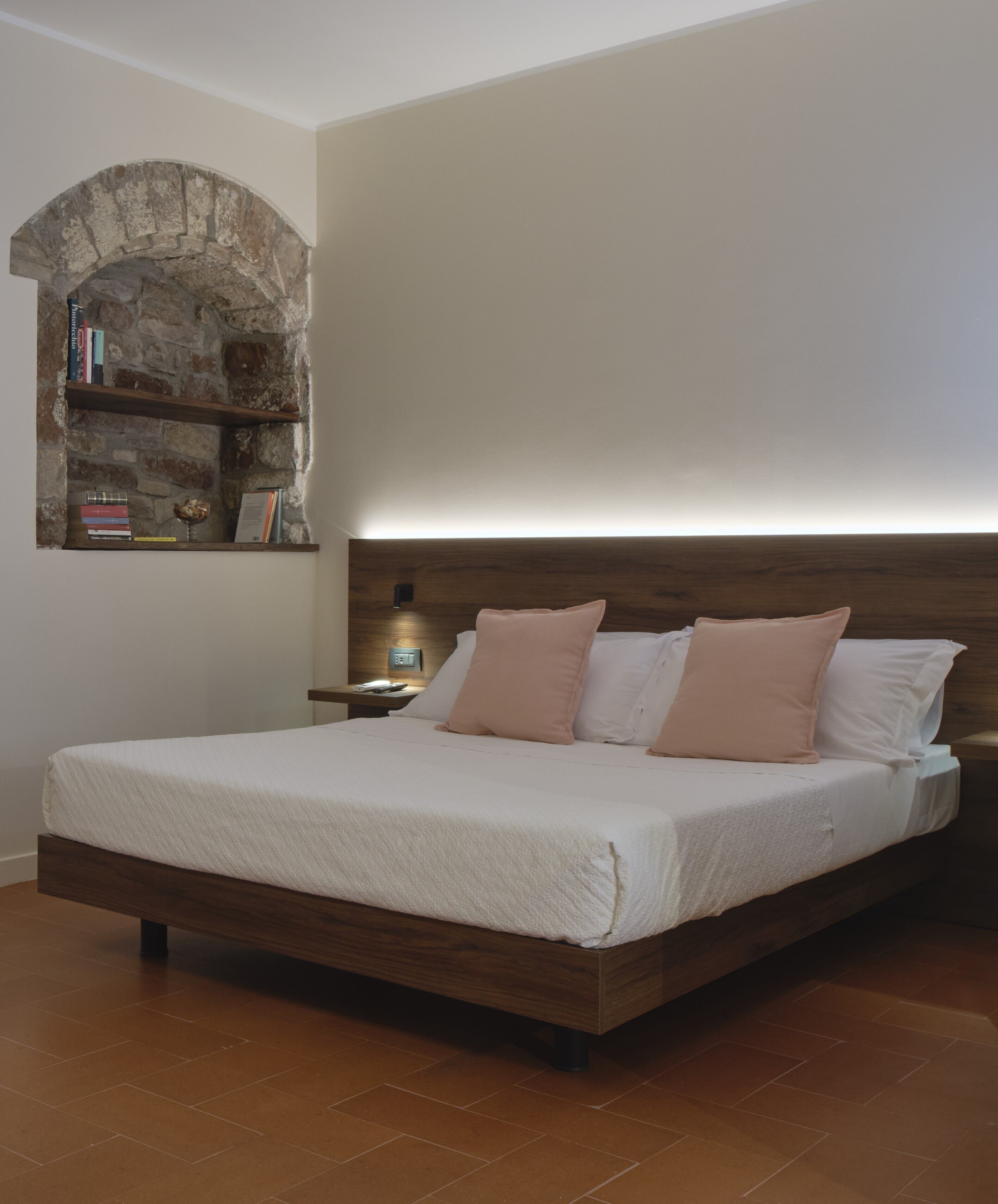 A bedroom with a wooden bed, a nightstand, a stone arch wall, and a bookshelf.