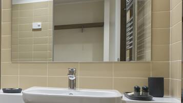 Un baño con lavamanos blanco, un espejo y azulejos color beige.