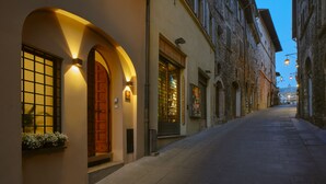 A narrow street with a building featuring an arched entrance and a wooden door. - Portica Homes Assisi (Assisi)