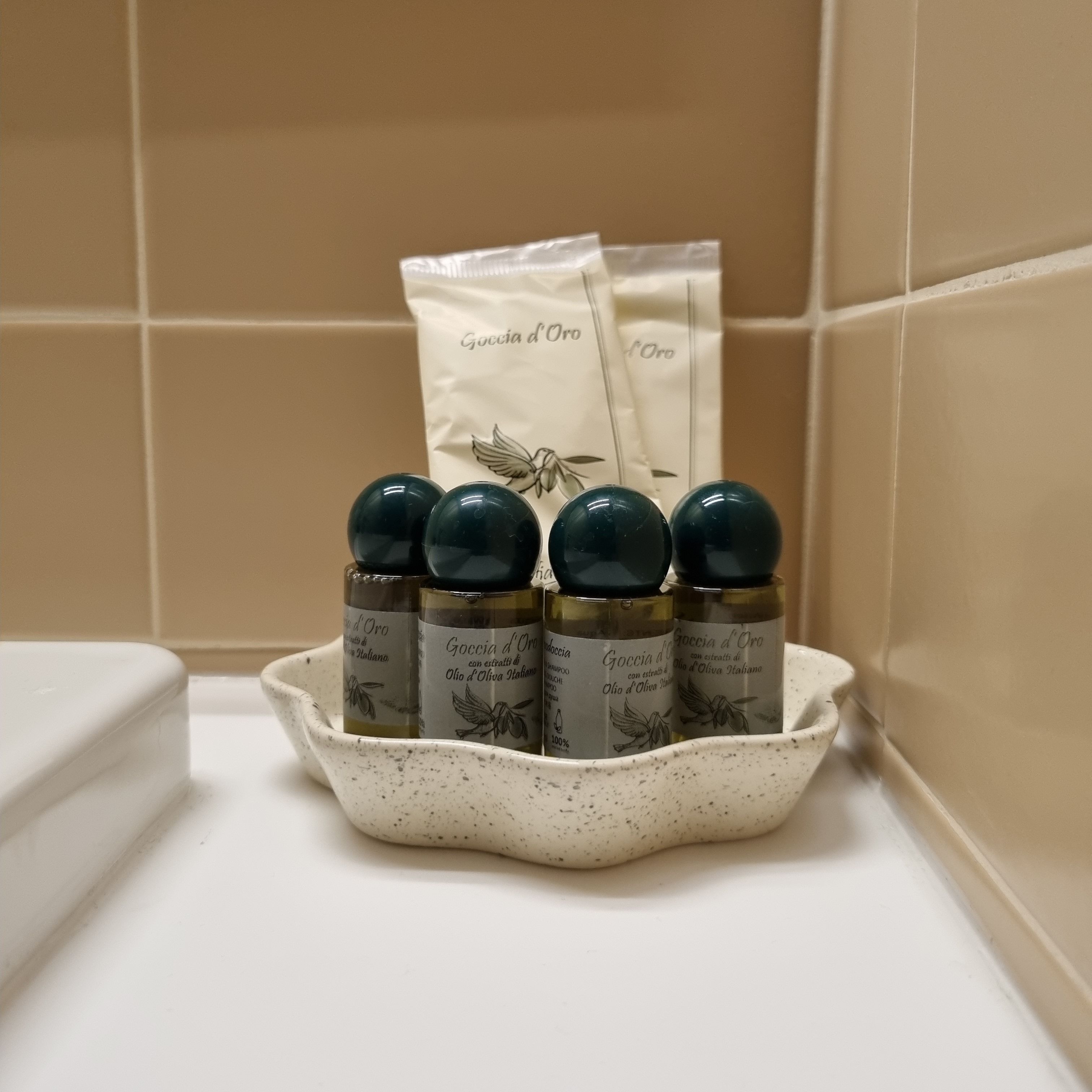 A white ceramic dish containing six bottles of Goccia d'Oro shampoo, with a white towel in the background.