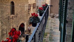 Une rue étroite bordée d’immeubles en pierre, un balcon orné de plantes en pot et un restaurant avec une terrasse.