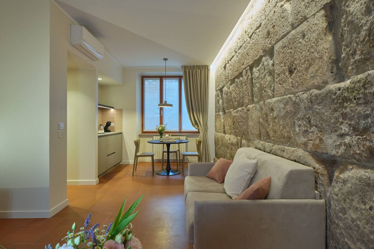 A modern living room with a stone accent wall, a dining area with a round table, and a kitchen in the background.
