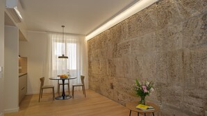 Un salon moderne avec un mur d’accent en pierre, une table de salle à manger ronde entourée de chaises, une petite table d’appoint avec un vase, et un coin cuisine en arrière-plan.