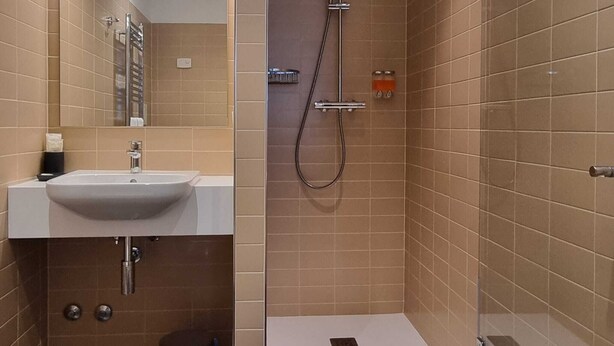 A modern bathroom with a sink, mirror, and shower. - Portica Homes Assisi (Assisi)