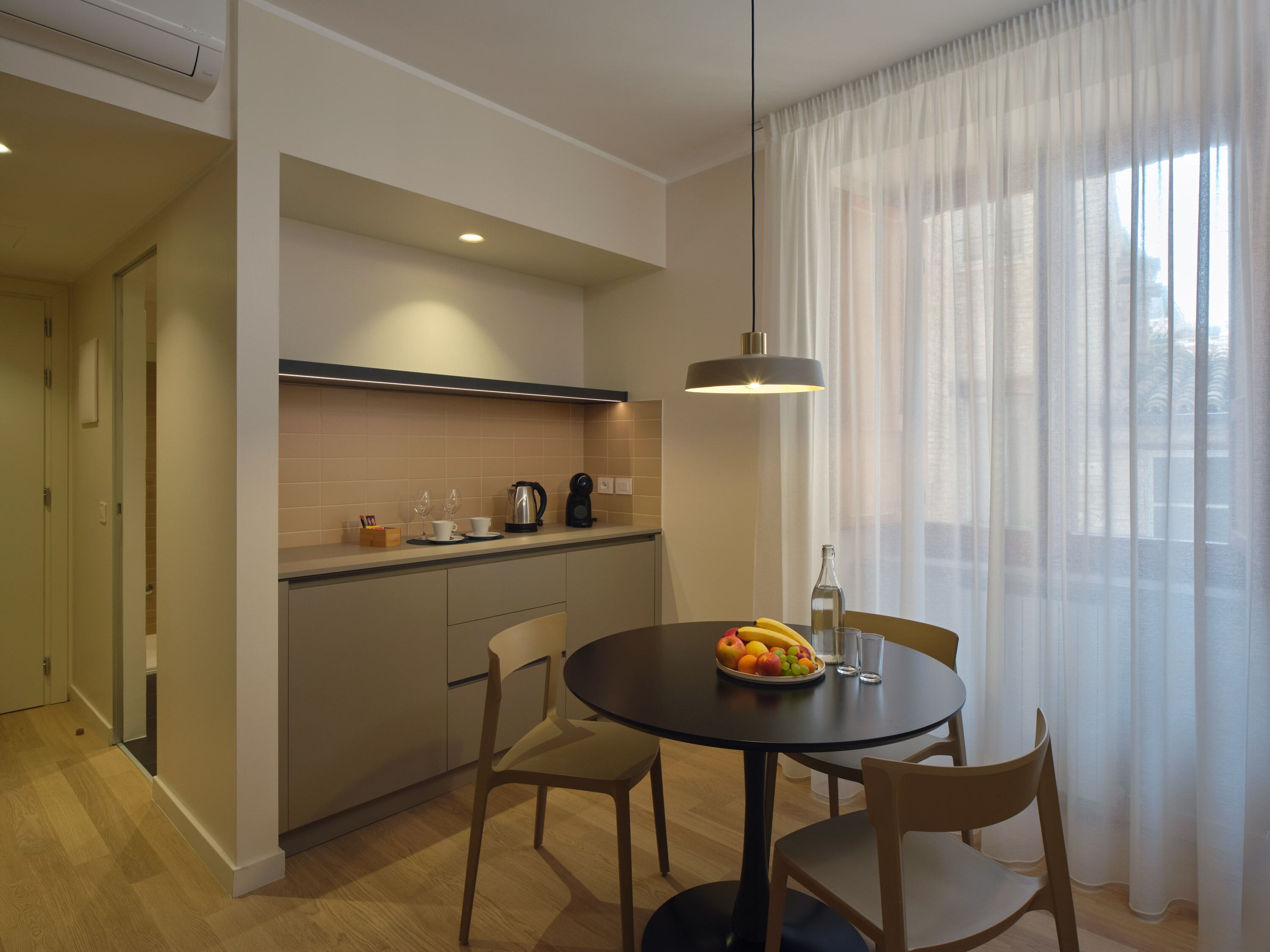 Une cuisine moderne avec un coin repas, comprenant une table ronde avec des chaises, un panier de fruits et une machine à café.