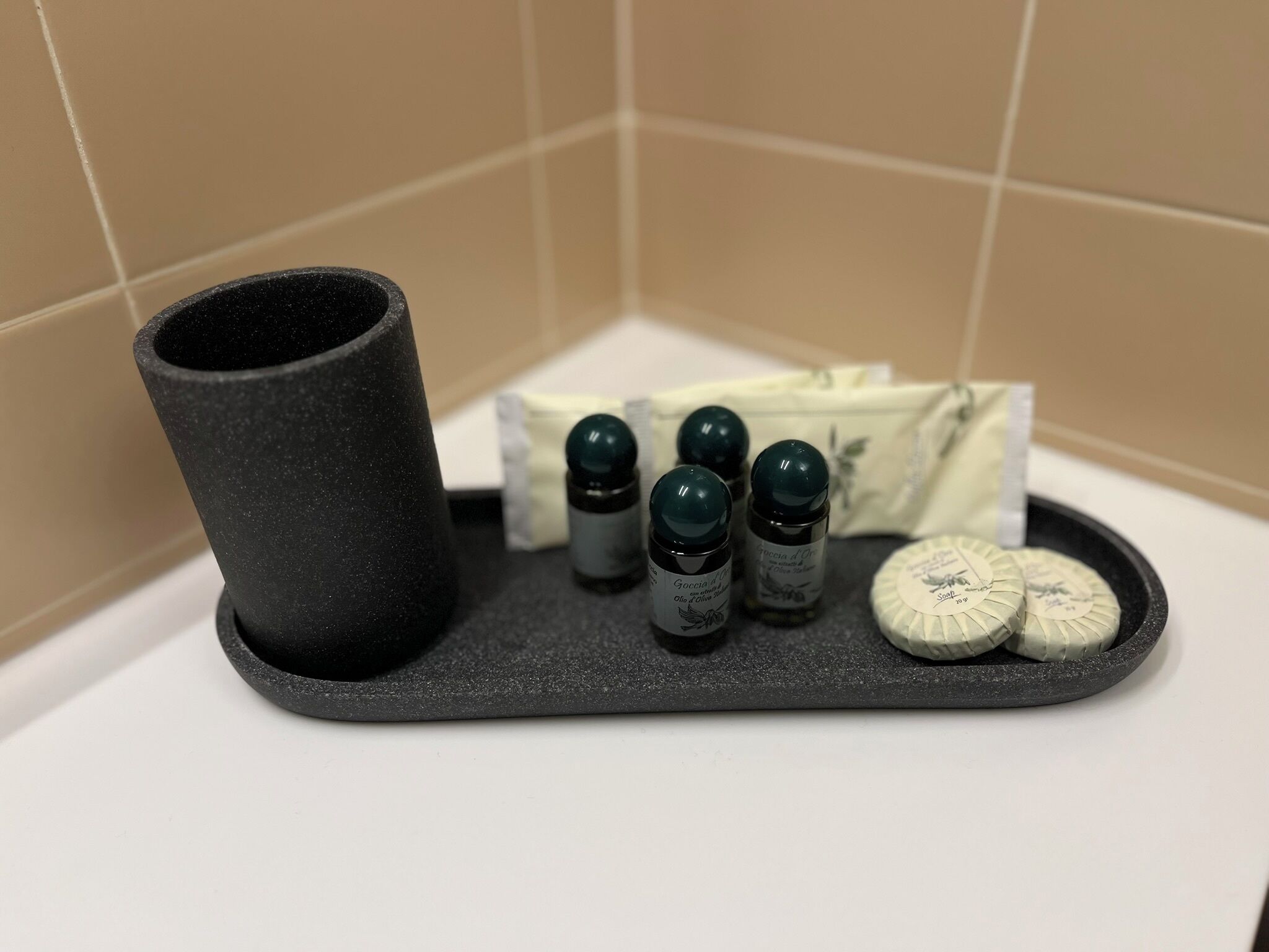 A bathroom with a black tray holding a black container, three small bottles, and two soap bars.