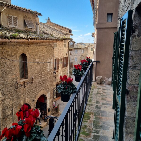 A narrow street with stone buildings, a balcony with potted plants, and a restaurant with outdoor seating.
