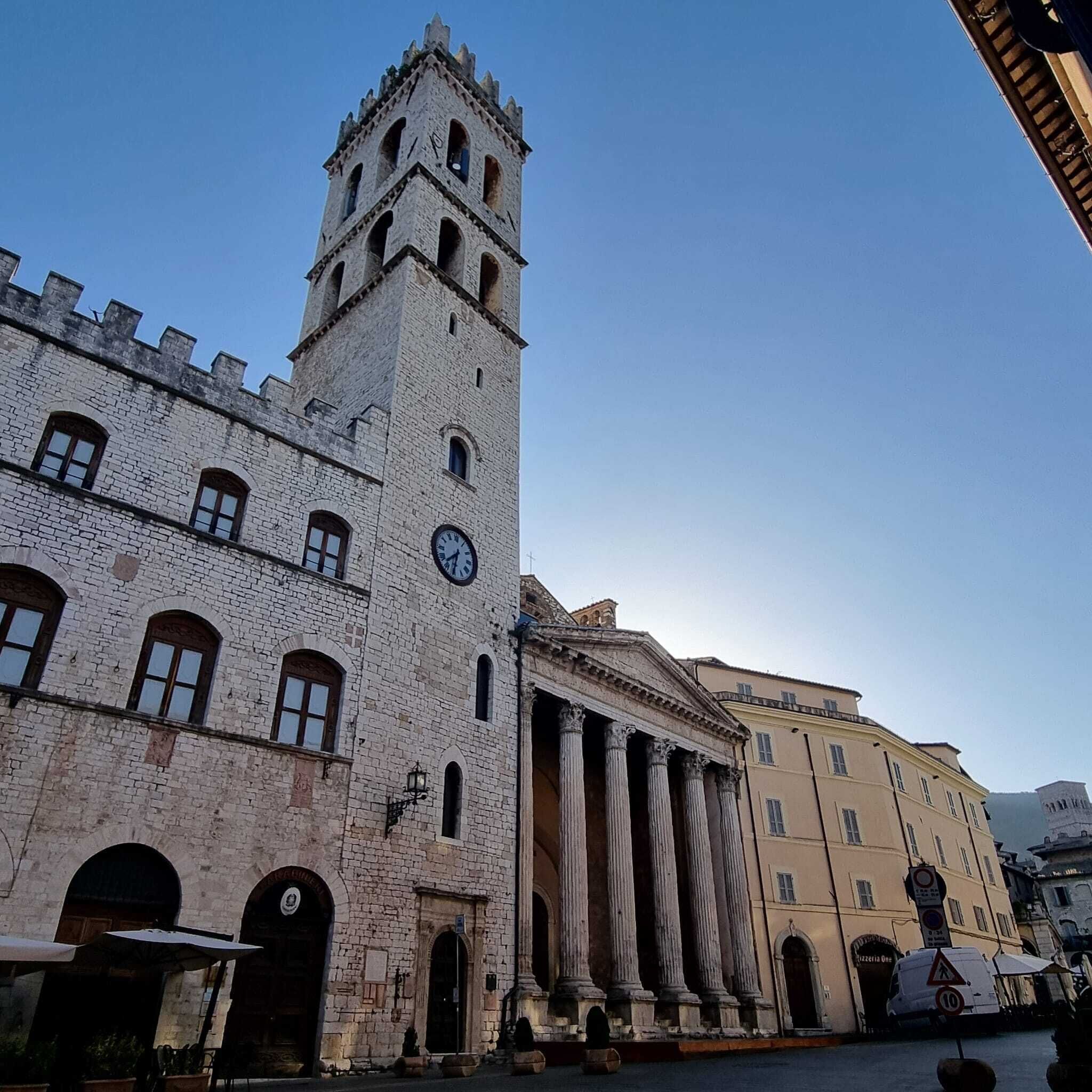 Un edificio histórico con una torre de reloj, columnas clásicas y una calle en primer plano.