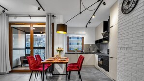 A modern kitchen with a dining area, featuring a wooden table, red chairs, and a pendant light.
