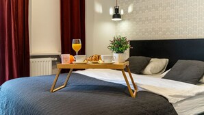 A neatly made bed with a tray of breakfast items, including croissants, a cup of coffee, and a glass of orange juice, set on a wooden stand.